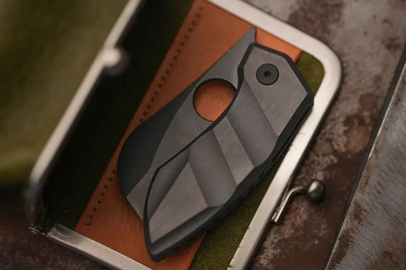 A modern folding knife with a sleek design lies on a textured leather surface, offering a rugged aesthetic