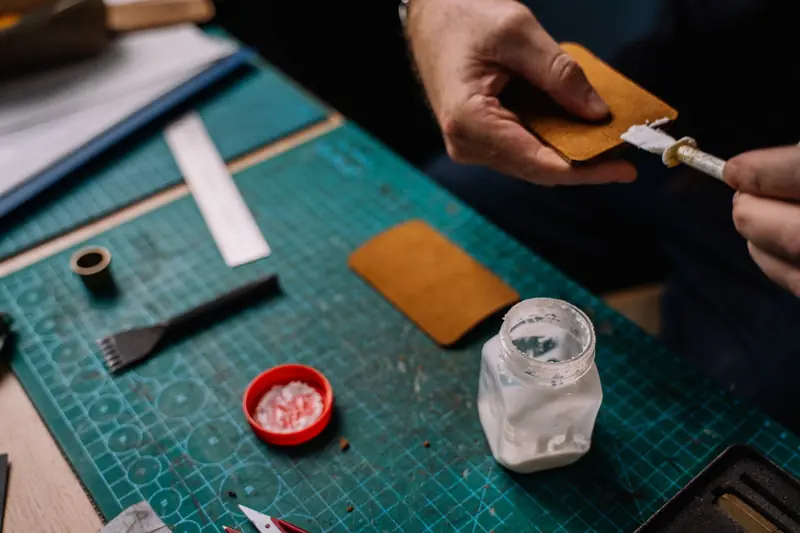 A detailed close-up of a person applying glue on leather for crafting purposes, showcasing handwork and tools