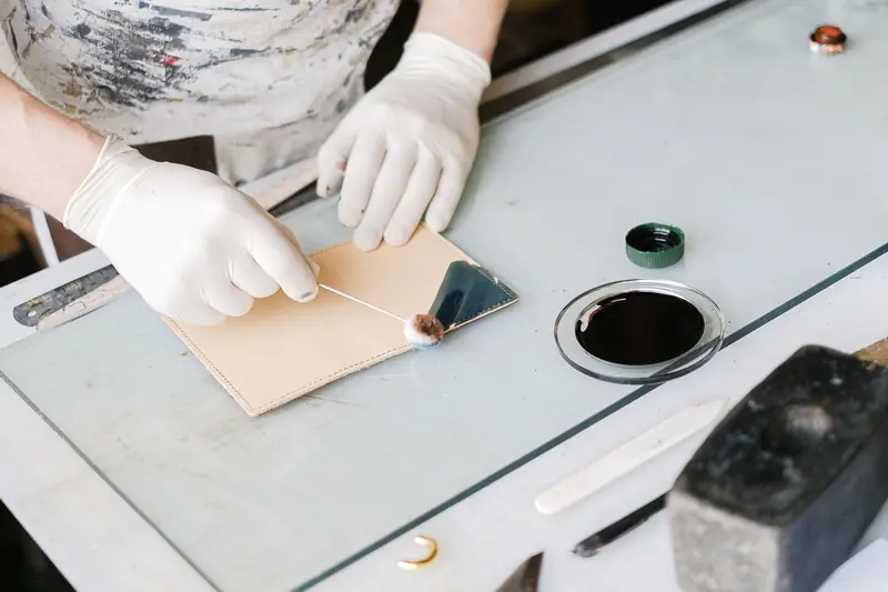 Close-up of gloved artisan hands applying ink to leather piece on a worktable, showcasing craftsmanship