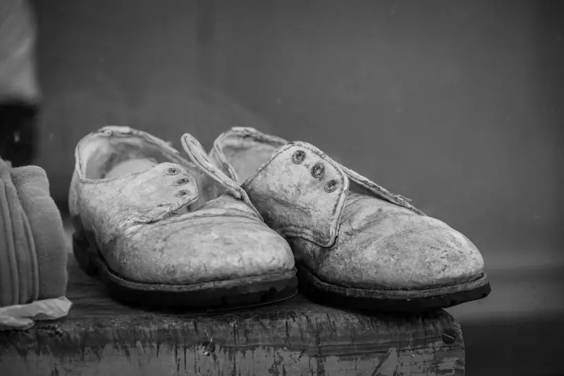 Black and white photograph of vintage worn leather shoes resting on a wooden surface, showcasing age and history
