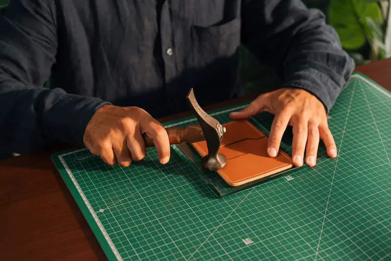 Artisan precisely crafting leather product with hand tools on cutting mat