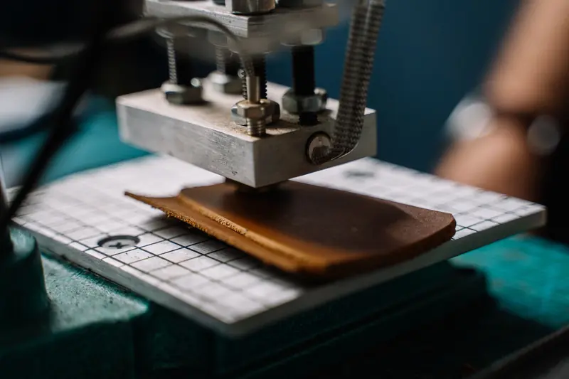A close-up image showing a machine cutting leather in a workshop setting