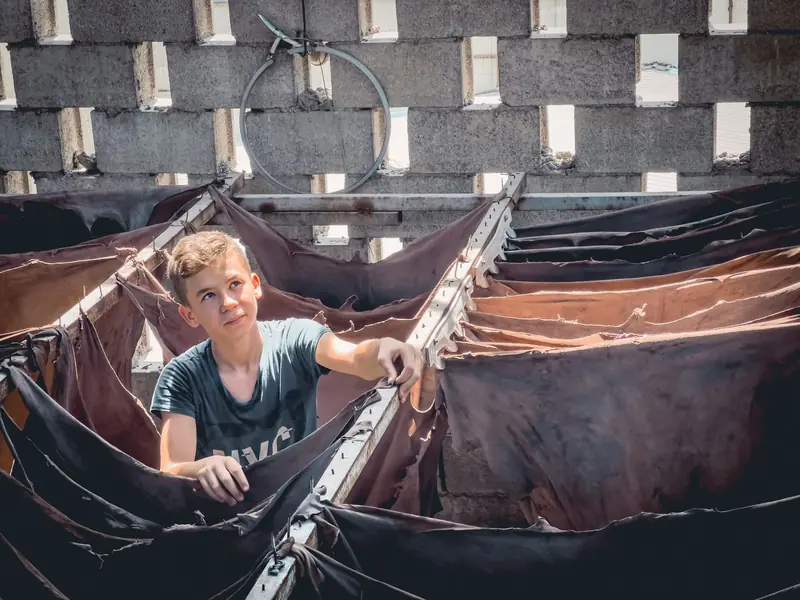A young boy inspects leather hides in a sunlit workshop, showcasing traditional tanning