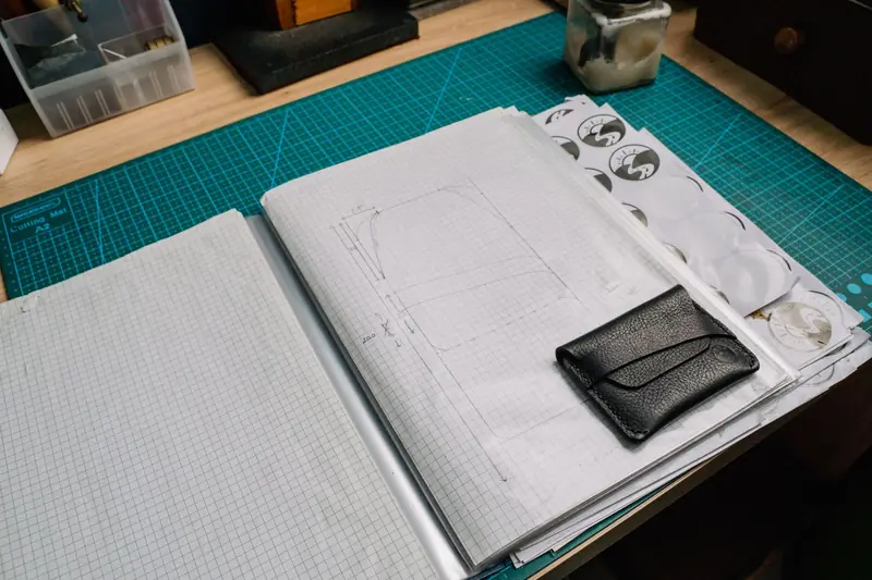 A creative workspace featuring a grid notebook, leather wallet, and various tools