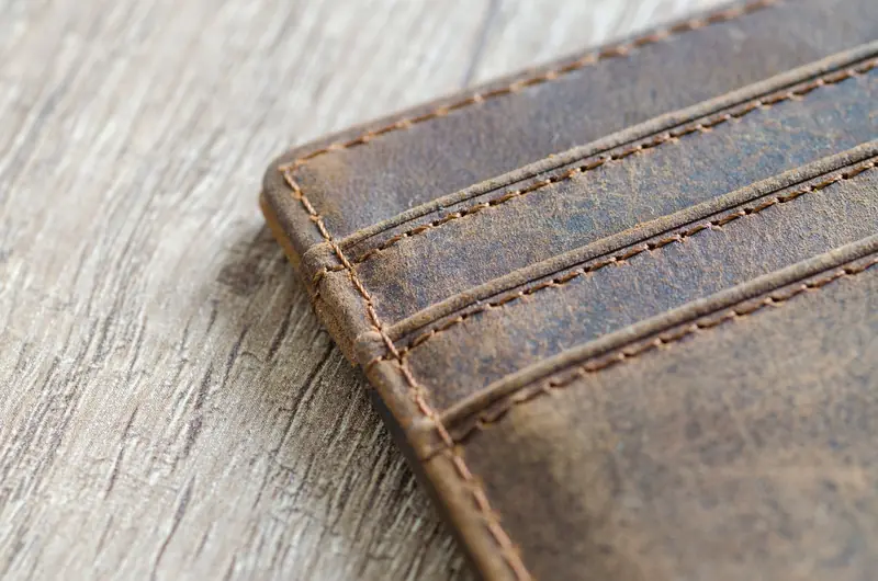 Detailed shot of a brown leather wallet on a textured wooden surface, showcasing stitching