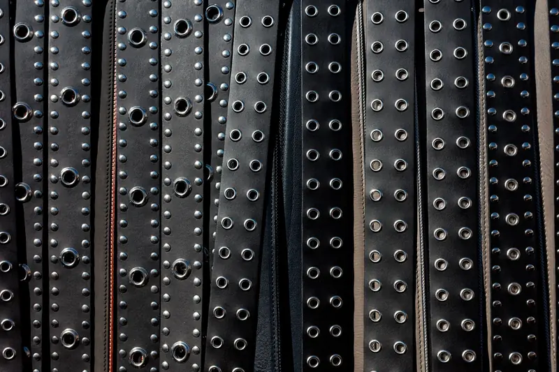 Close-up view of multiple black leather studded belts arranged in rows