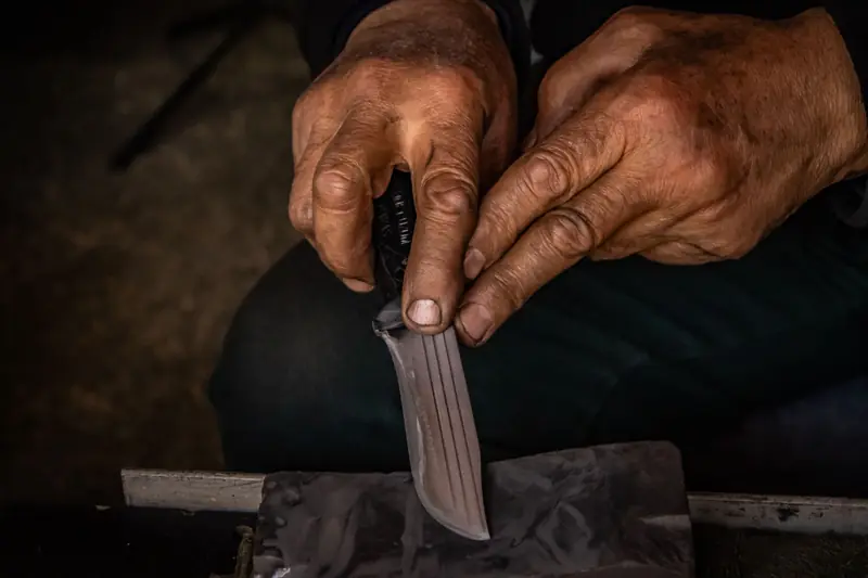 Detailed image of hands sharpening a knife using a whetstone, showing craftsmanship and precision