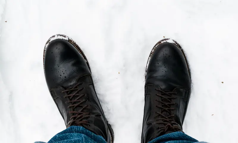 A pair of black leather boots stand in fresh snow, captured in Oslo during winter