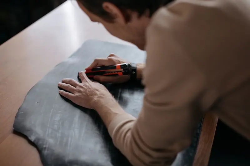 Close-up of an artisan using a utility knife to work on a leather piece at a table