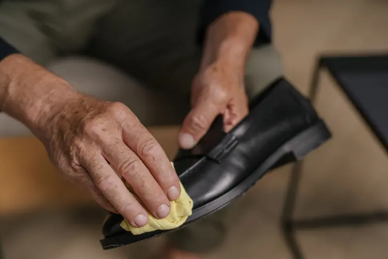 Detailed image of hands polishing a black leather shoe with a yellow cloth, emphasizing care and maintenance