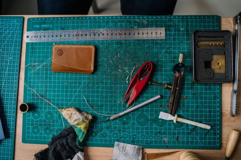 Top view of leather crafting tools including ruler, scissors, and wallet on a work table