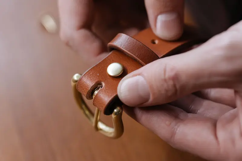 Detailed shot of hands holding a brown leather belt with a buckle