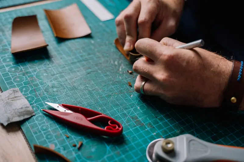 Detailed view of leather crafting with tools and hands on cutting mat, showcasing artisan skill