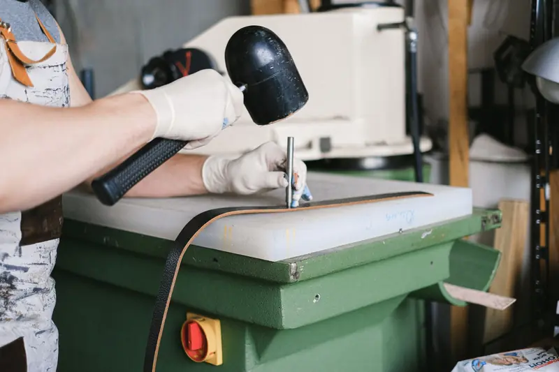 A leather artisan uses a mallet to craft leather goods on a workbench