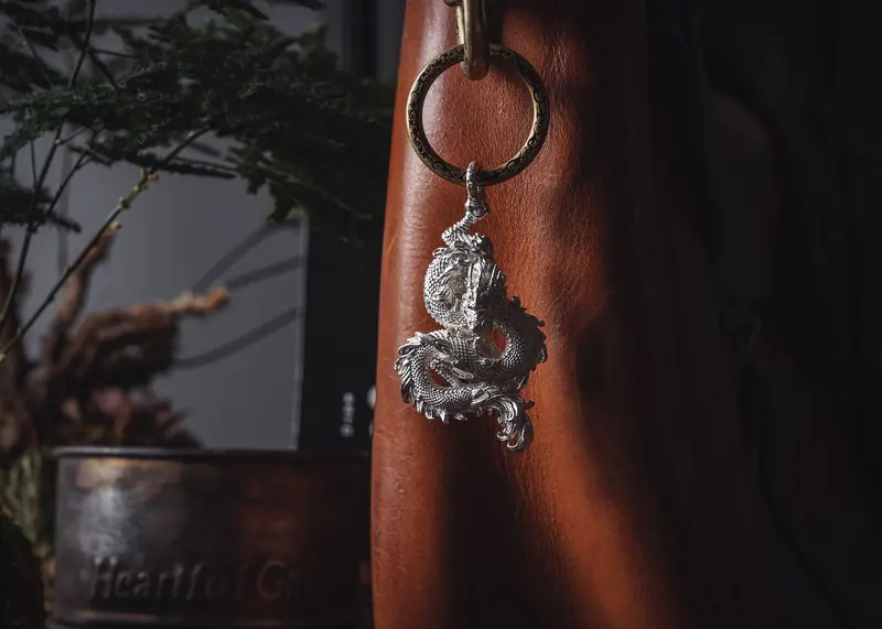 A silver dragon keychain displayed on a luxurious brown leather bag in a cozy setting